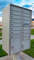 Vertical frame White metal cluster mailbox with pond grassy terrain and homes in the background