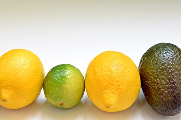 Close up of lemons, lime and avocado in a row on white background.