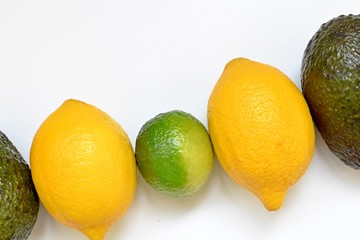 Top table with lemons, lime and avocado in a diagonal row on white background.