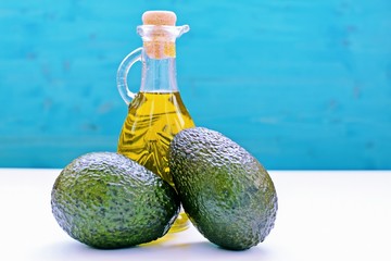 Concept with avocados and a bottle of olive oil on blue and white background.