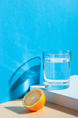 On a yellow-blue background, a glass with water, lemon and orange. Fresh summer still life with water and tropical fruits
