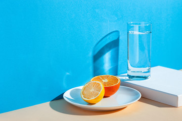 On a yellow-blue background, a glass with water, lemon and orange. Fresh summer still life with water and tropical fruits