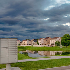 Square Sky filled with gray clouds over homes and pond amid a vast grassy terrain