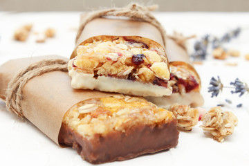 Fototapeta na wymiar Granola bar on white table. Healthy organic sweet dessert snack. Cereal granola bar with nuts and dried fruits wrapped in paper.