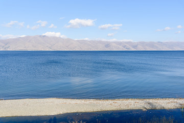 the endless expanses of water of Lake Sevan on a sunny day with clouds in the sky and mountains on the horizon. Location in Armenia