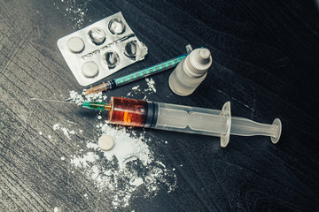 Syringe with drugs (heroin) and pills and powder on the table. Drug addiction.