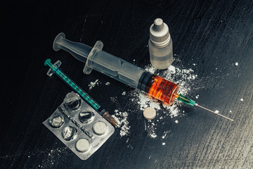 Syringe with drugs (heroin) and pills and powder on the table. Drug addiction.