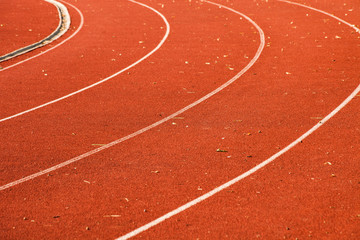 closeup of athletic red running tracks whit white lines and some leaves on it