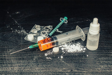 Syringe with drugs (heroin) and pills and powder on the table. Drug addiction.