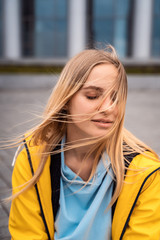Beautiful young blonde woman on the street, posing with wind in her hair