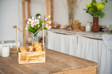 Bread in a textured wooden box in the kitchen in a rustic style. Breakfast, bread, white cups in the interior of bright Scandinavian cuisine.