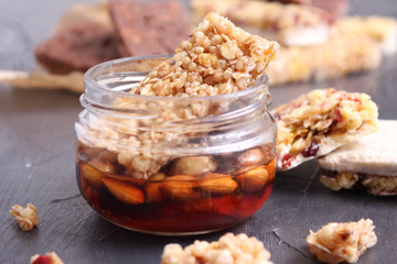 Granola bar on black table. Healthy organic sweet dessert snack. Cereal granola bar with nuts and dried fruits inside a jar with honey and nuts.
