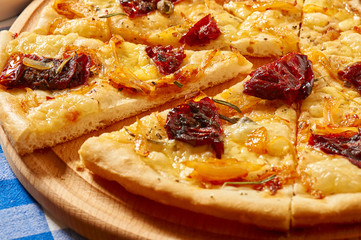 Pizza with dry tomatoes, onion and cheese on a wooden plate