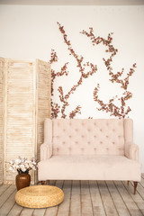 Pink vintage sofa and screen in rustic style. Interior of a bright Scandinavian living room with flowers on the wall.