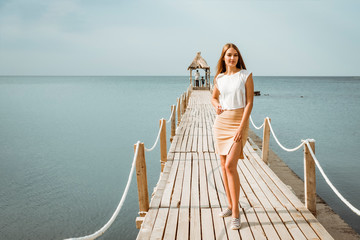 Girl on the pier with a bungalow on the background of the sea.