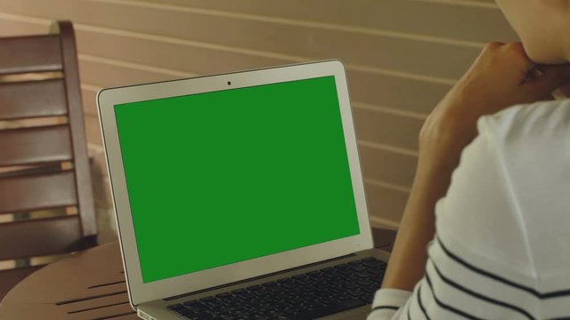 Over the shoulder shot of Asian woman looking at green screen. Office person using laptop computer with laptop green screen,