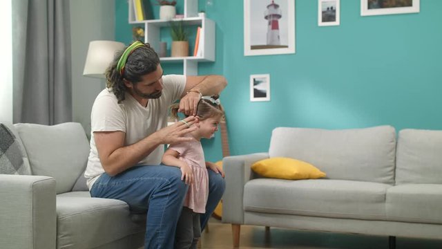 Young bearded father brushing the hair of his little girl and makes the tail