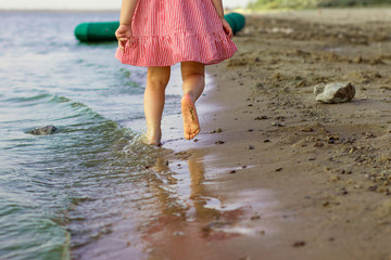 little girl runs barefoot along the beach with spray on the water