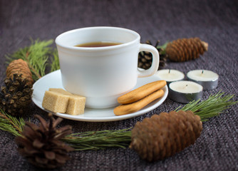 Cup of fragrant hot tea among Christmas tree branches and pine cones on a plaid.
