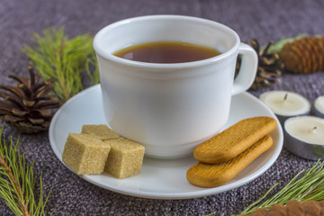 Cup of fragrant hot tea among Christmas tree branches and pine cones on a plaid.