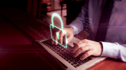 Man typing on laptop with padlock hologram screen over keyboard. Cyber security, computer protection and internet safety concept.