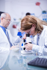 Senior female scientist doing medical research looking at sample under a microscope