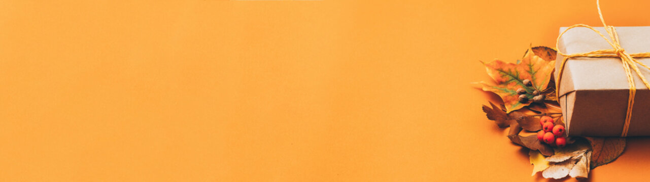 Autumn holiday decor. Beige handmade paper gift box with yellow leaves on orange background. Copy space.