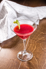 Sweet summer strawberry alcoholic cocktail with lime peel in martini glass on wooden table