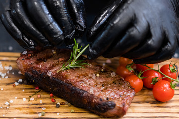Steakhouse menu. Striploin steak. Closeup of chef hands serving grilled beef meat with cherry...