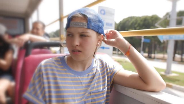 Sad teenage girl in a baseball cap riding on a bus with no Windows.