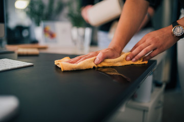 Wiping black desk with cloth, close-up.
