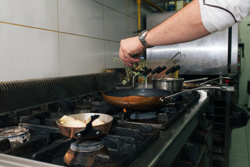 Hand of a chef adding herbs to a meal on a stove.