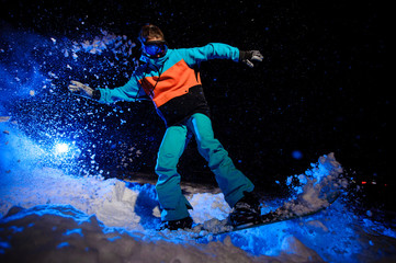 Female snowboarder dressed in a orange and blue sportswear jumping on the mountain slope