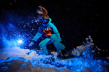 Active female snowboarder dressed in a orange and blue sportswear jumping on the snow slope