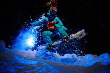 Obraz na płótnie Canvas Female snowboarder dressed in a orange and blue sportswear performs tricks on the snow