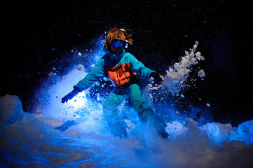 Obraz na płótnie Canvas Active female snowboarder dressed in a orange and blue sportswear performing tricks on the snow