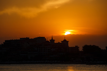 Golden sunset on the beach. Silhouette of the city. Beautiful architecort by the sea on the background of the sunset.