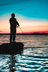 Silhouette of a fisherman staying on a rock after sunset