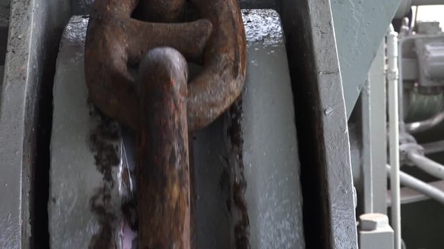 brown rusty anchor chain moves down by winch with several snaps on grey special wheel support on ship close view