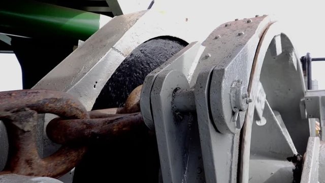 special rotating grey metal winch wheel lifts up brown rusty anchor chain with snaps close view