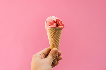 The girl holds ice cream in her hand in a cup on a pink background.
