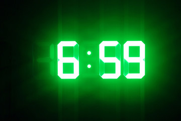 Green glowing digital clocks in the dark show 6:59 time