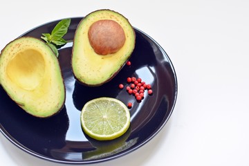 Black plate with raw avocado and a slice of lime on white background. Top table with copy text.