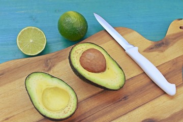 Top dish with a cut avocado, limes and a knife on wooden plate and blue background.