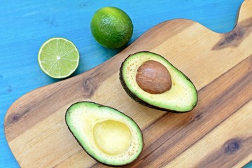 Top dish with a cut avocado, limes on wooden plate and blue background.