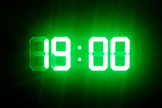 Green glowing digital clocks in the dark show 19:00 time
