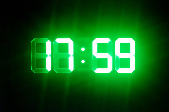 Green glowing digital clocks in the dark show 17:59 time