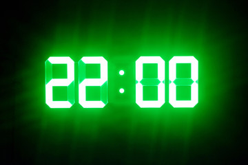 Green glowing digital clocks in the dark show 22:00 time