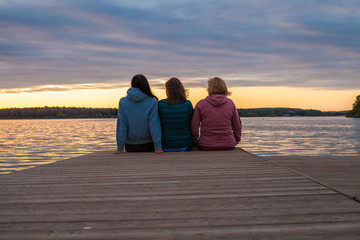 Three girls admire the sunset sitting on the pier