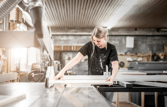 junge Frau schneide eine Holzplatte an der Formatkreissäge in der Schreinerei